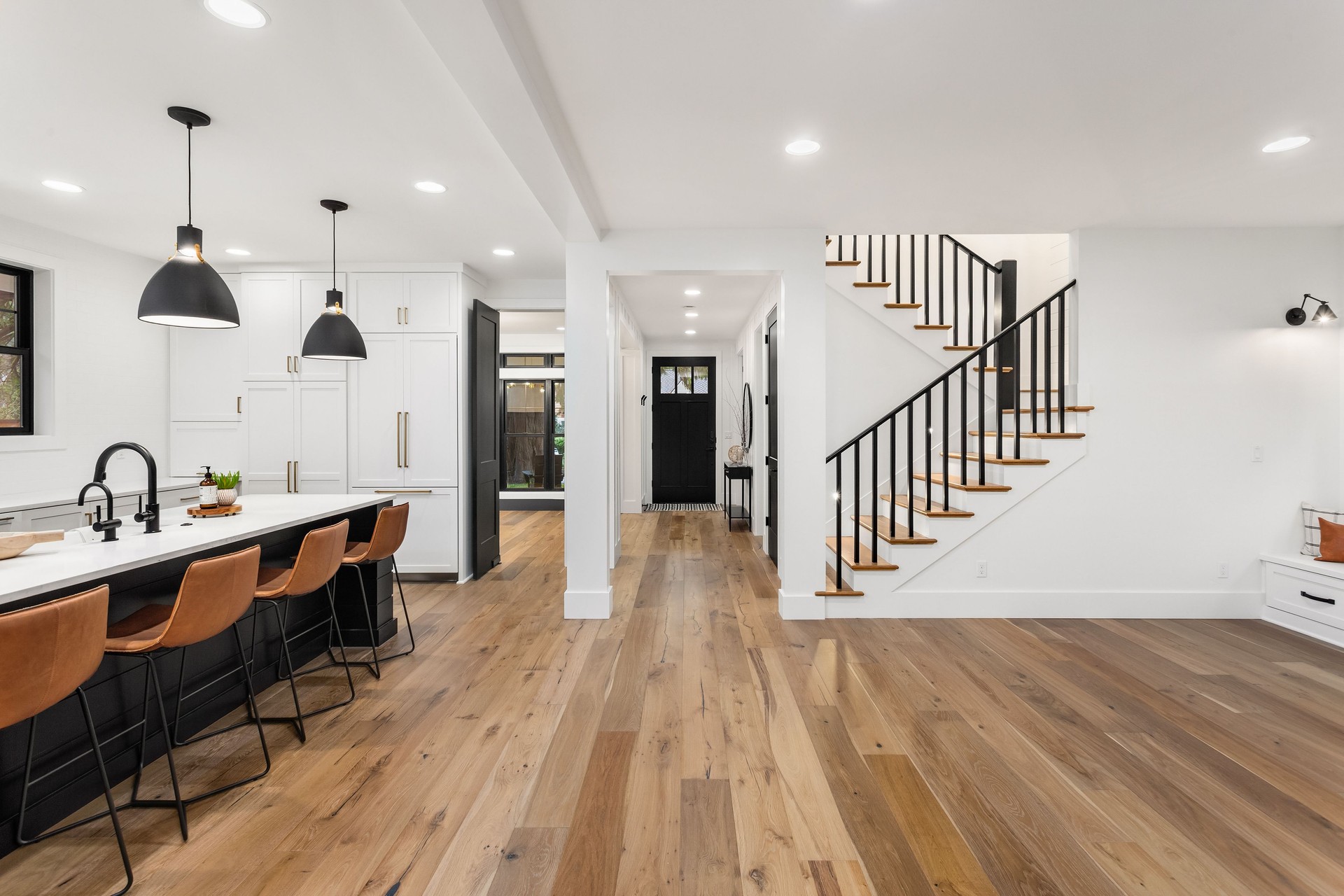 Cuisine et salon intérieur dans une nouvelle maison de luxe de style ferme avec plan d’étage à aire ouverte. Comprend une grande île avec évier de ferme, planchers de bois franc et accents noirs.